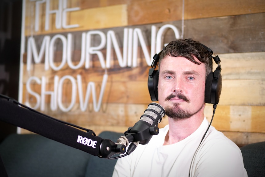 a man with brown hair, a mustache and blue eyes is in front of a microphone