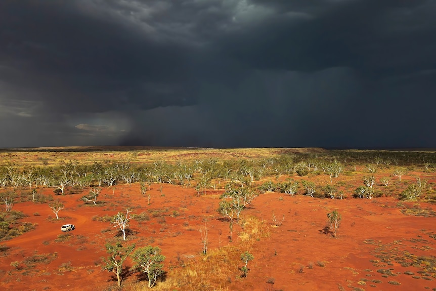 Dark grey skies over a red dirt country with Kylie's car in the distance