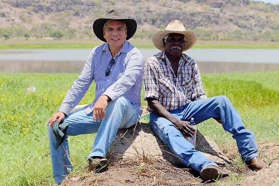 two Indigenous man sitting out near a lake on a rock under the sun