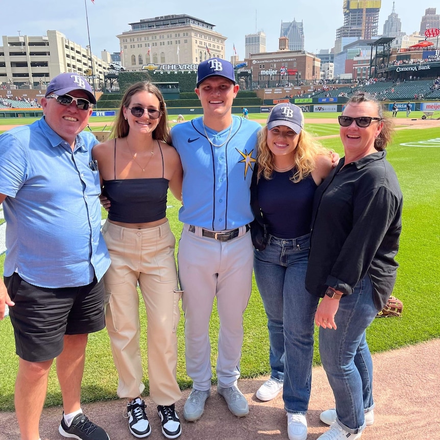 family posing with baseballer with baseball diamond in background