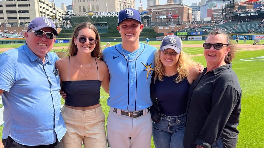 family posing with baseballer with baseball diamond in background