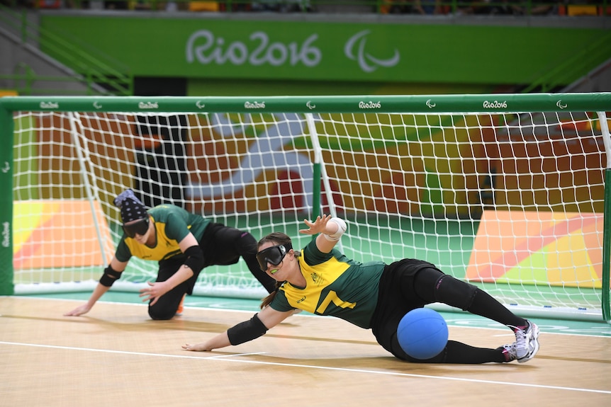 Two members of the Australian women's goalball team lie horizontal to stop the ball from entering the goal.