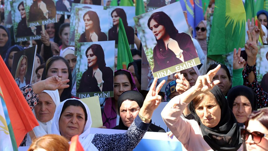 Iranian women demonstrate holding up photos of Mahsa Amini.