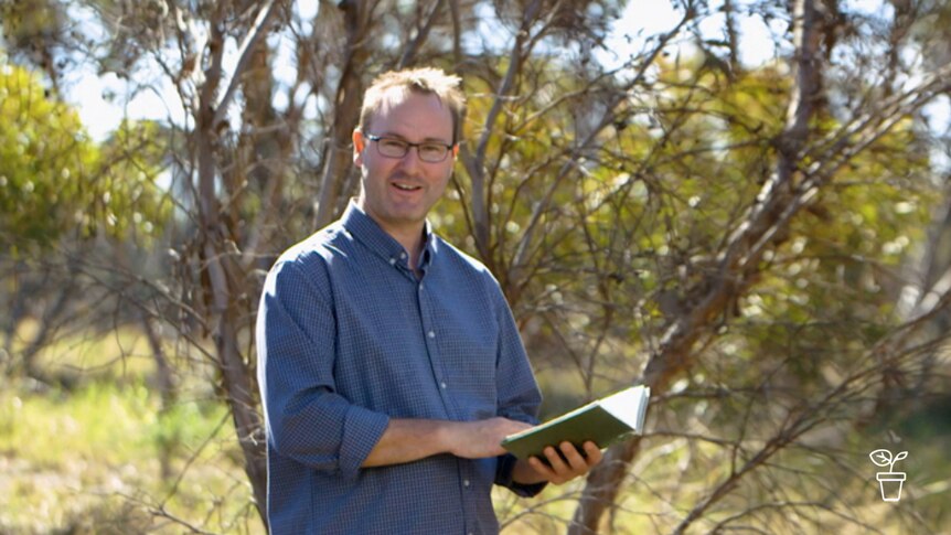 Man wearing glasses standing outdoors with book in hands