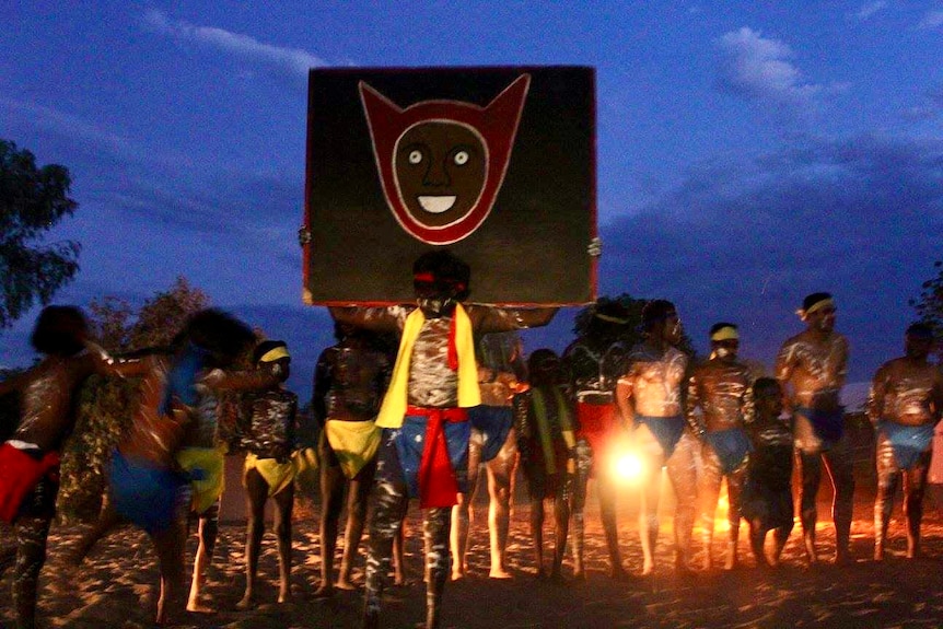 Aboriginal dancers hold a totem up high in the night sky during a performance