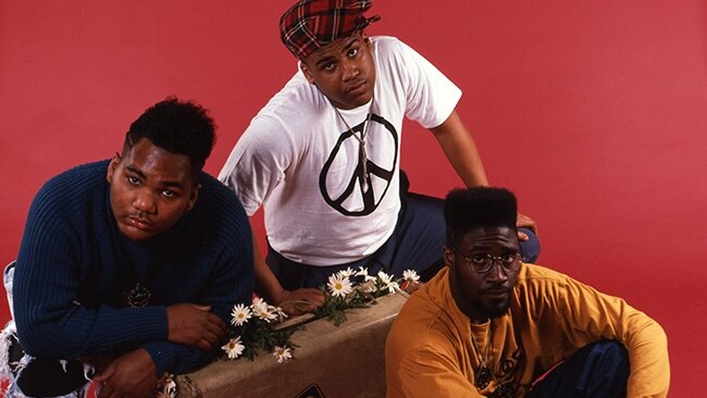 American hip hop trio De La Soul stand against a red backdrop