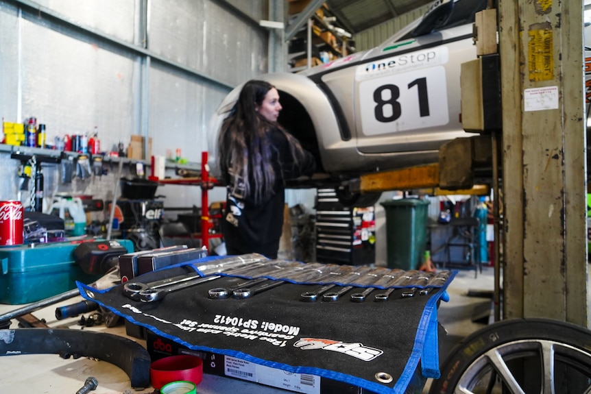 A woman fixes a car with mechanical tools in the foreground.