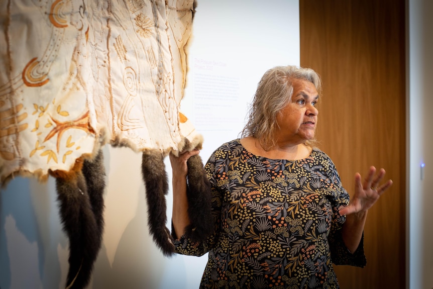 Loretta Parsley standing next to a possum skin cloak that's on display, and speaking.