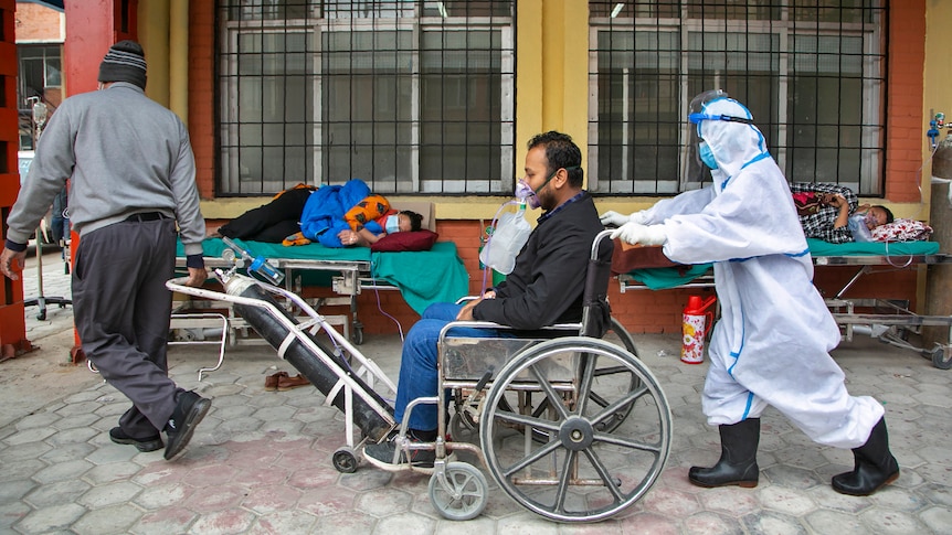 A COVID-19 patient arrives on a wheelchair as others are lying down on beds outside an emergency ward in Kathmandu.