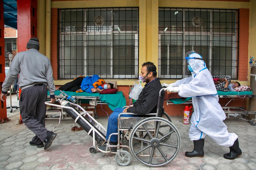 A COVID-19 patient arrives on a wheelchair as others are lying down on beds outside an emergency ward in Kathmandu.