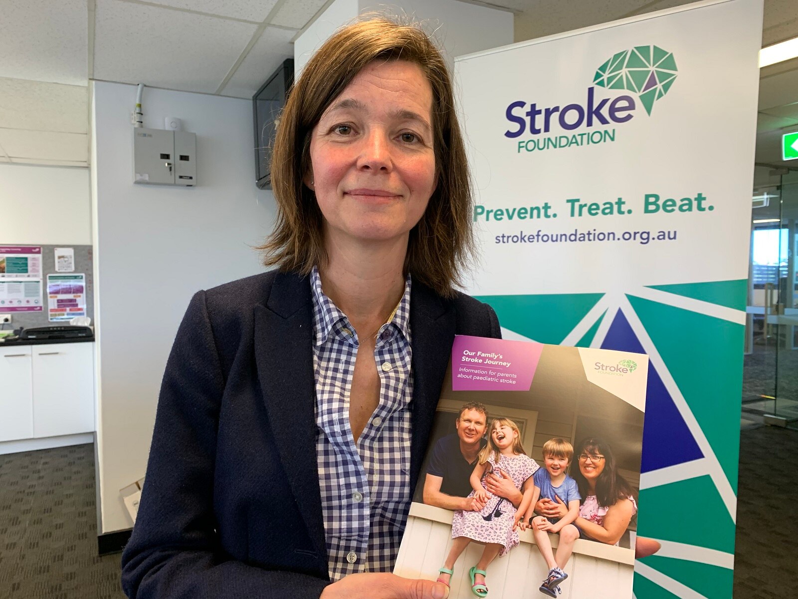Dr Lisa Murphy, brown hair, light brown eyes, holding a Stroke Foundation book, smiling at the camera.