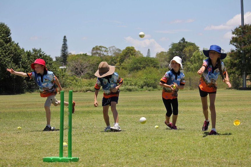 Children in matching polo shirts play cricket.