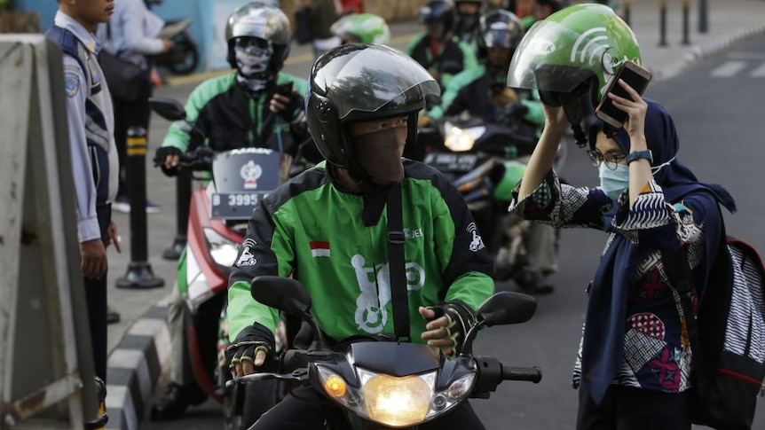 Indonesian people on motor scooters prepare to set off with their deliveries