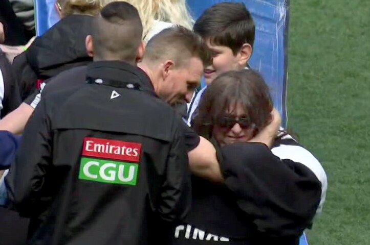 Collingwood supporter Voula Bitsikas is comforted by Nathan Buckley on the MCG oval after the team banner tore early.