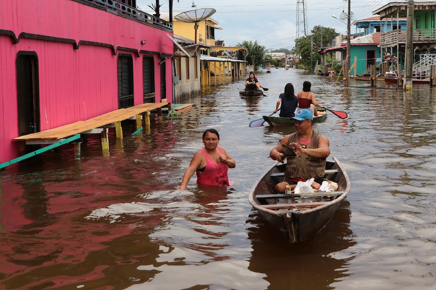 Residents wade through flooded streets, alongside other residents in boats.