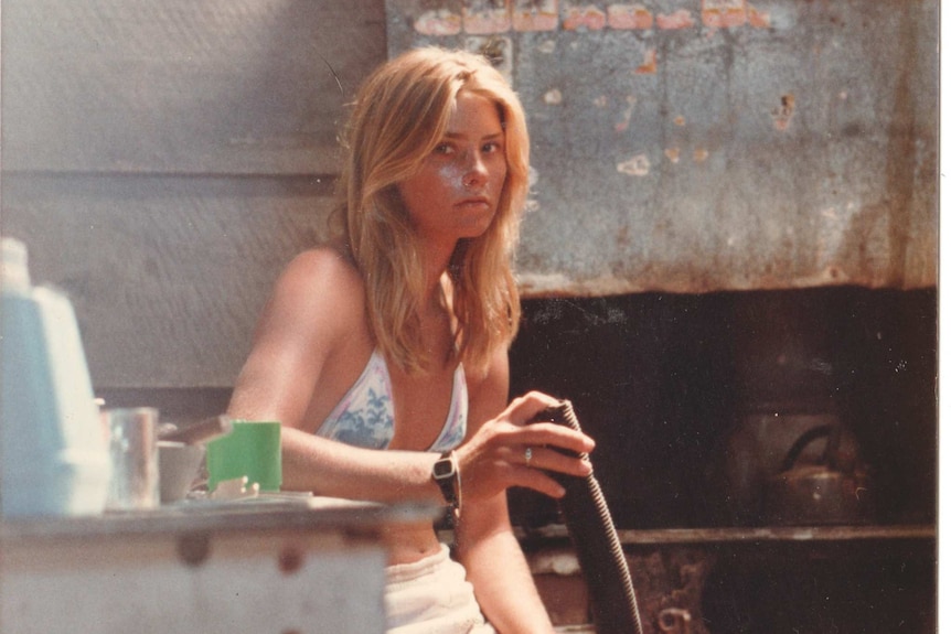 A blonde woman sitting at a desk and looking at the camera.