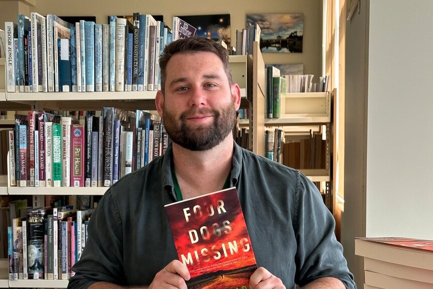 A man with a beard holding a novel, titled 'Four Dogs Missing'