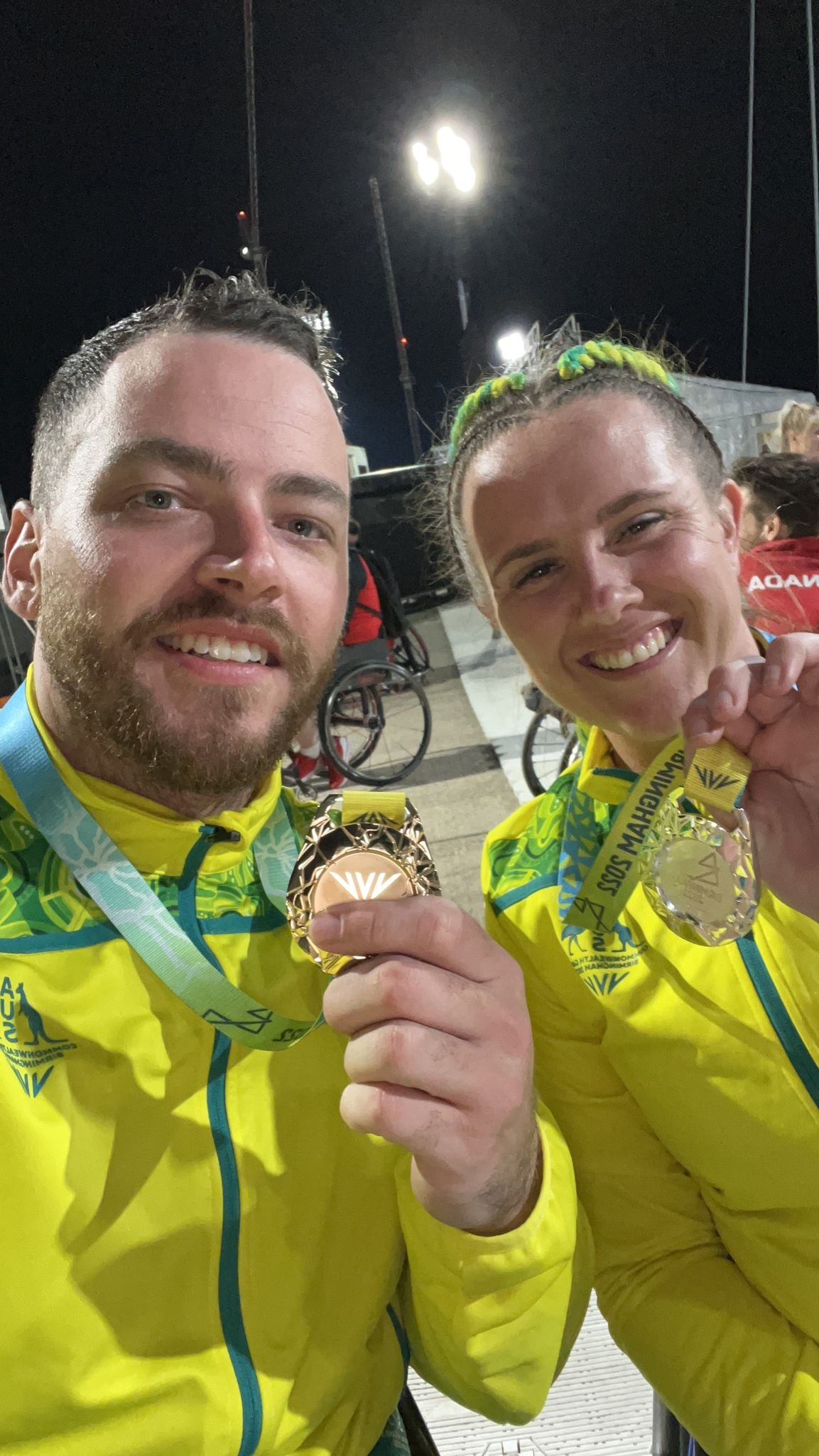Two para-athletes smile as they hold up gold medals.
