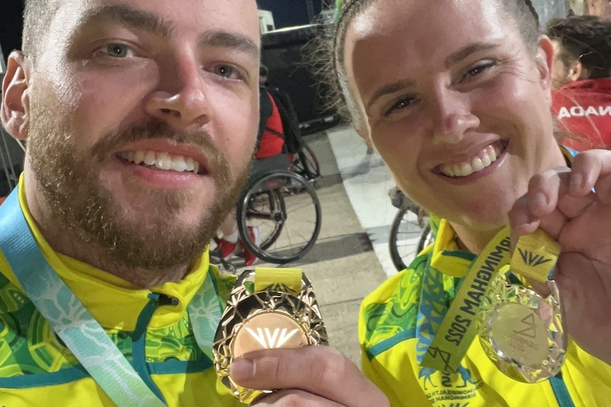 Two para-athletes smile as they hold up gold medals.