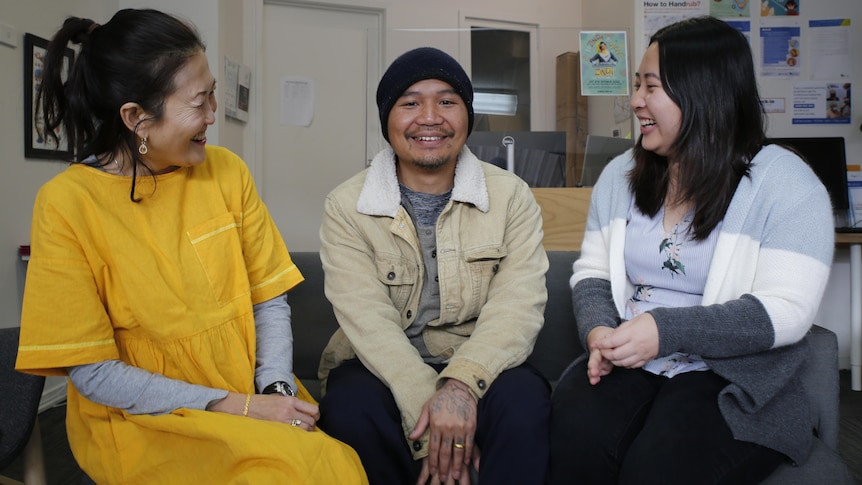 Three people smiling on a couch in an office.