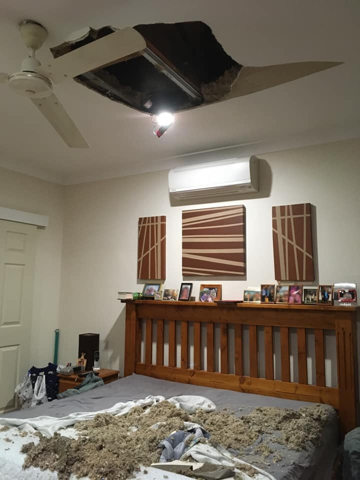 A bedroom in which the roof has fallen in with pieces of the roof scattered across a bed below
