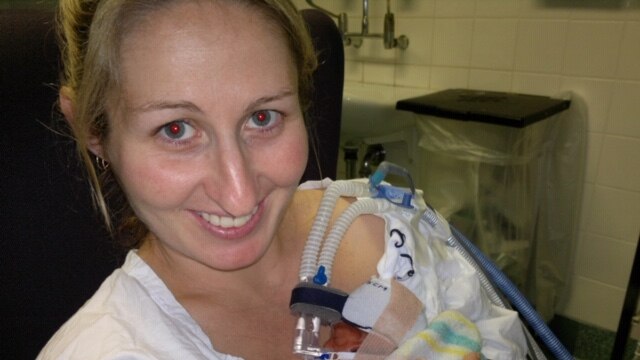 A woman in hospital with a premature baby resting on her shoulder.