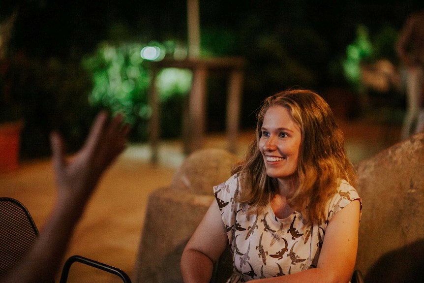 A woman smiles in conversation with someone.