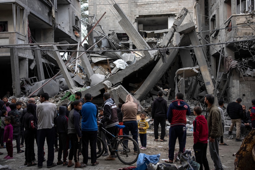 People huddle in front of the remains of a concrete building destroyed by a blast