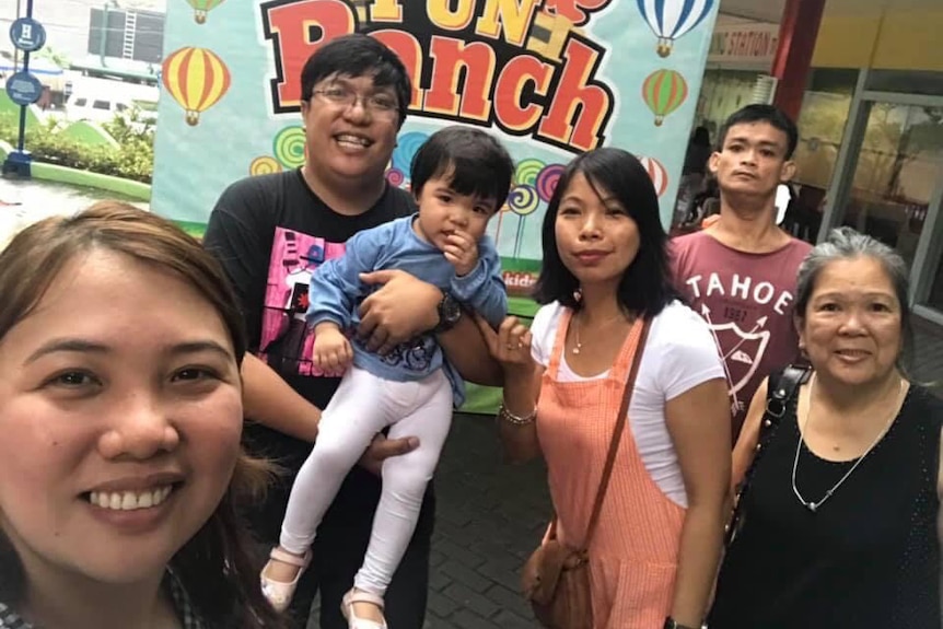 Three women and two men smile for the camera. One of the men holds a toddler.