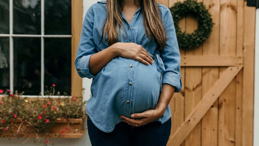 A woman in a denim shirt holding her pregnant belly