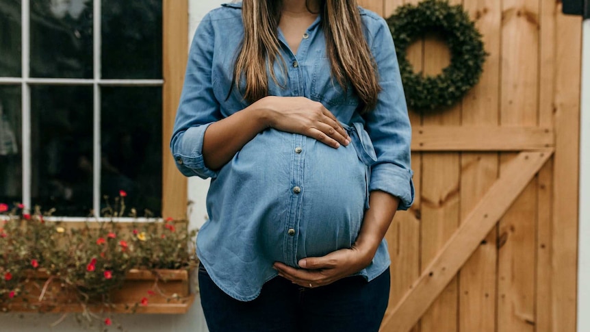 A woman in a denim shirt holding her pregnant belly
