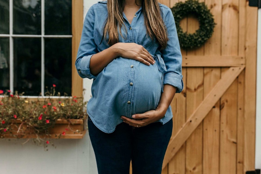 A woman in a denim shirt holding her pregnant belly