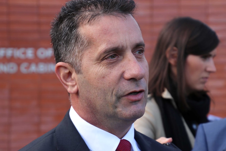 A tight head shot of WA Corrective Service Minister Paul Papalia speaking to reporters with a woman behind his left shoulder.