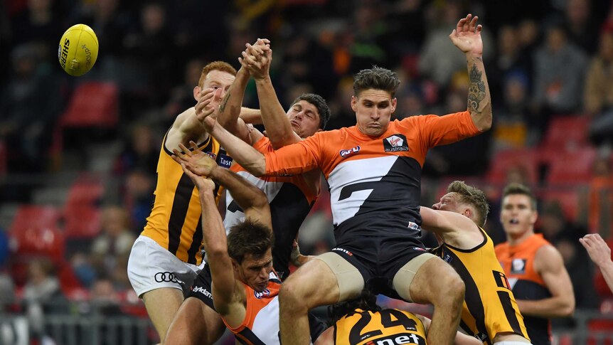 GWS Giants player Rory Lobb falls backwards onto Hawks player jumping for a loose ball