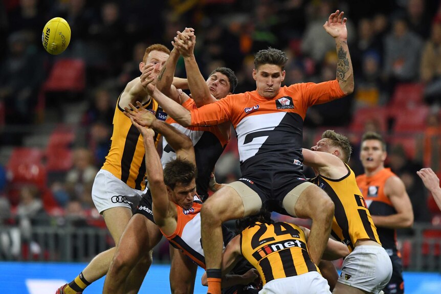 GWS Giants player Rory Lobb falls backwards onto Hawks player jumping for a loose ball