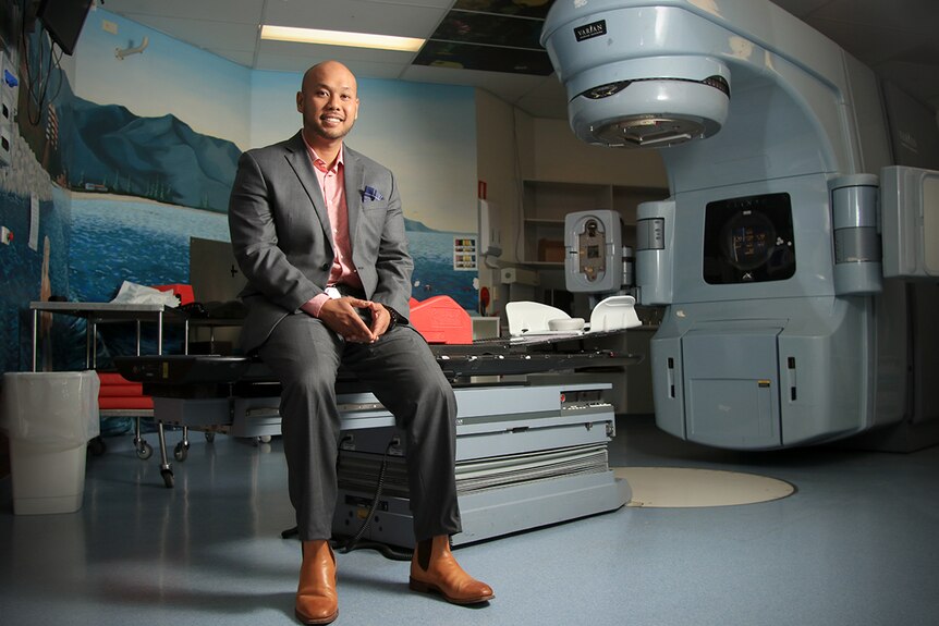 A man in a suit sits on machinery used to administer radiation therapy.