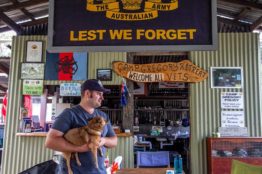 A man holds a dog in front of a camp kitchen