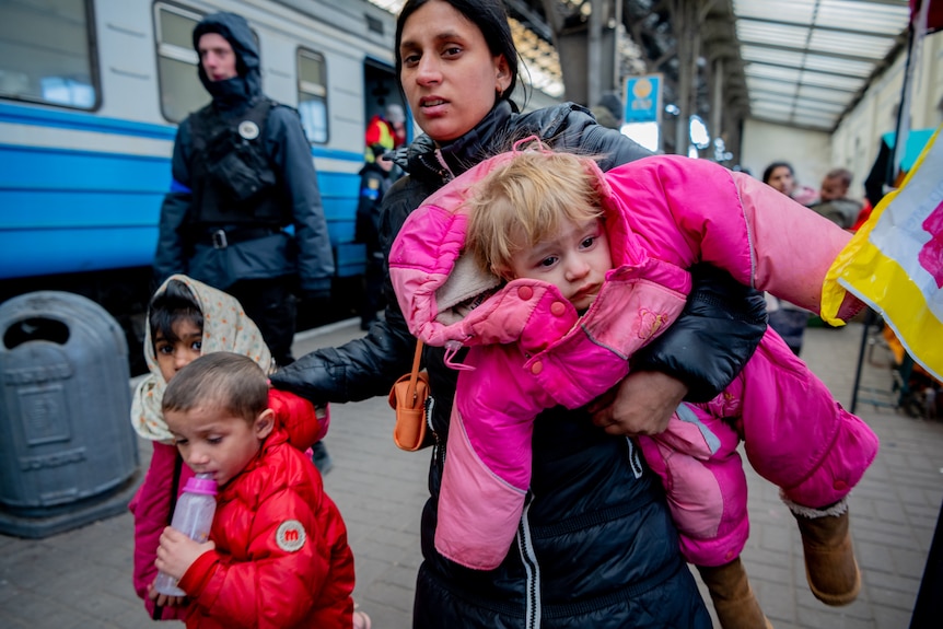 A young child in a pink full-body puffer suit is carried by their mum. 