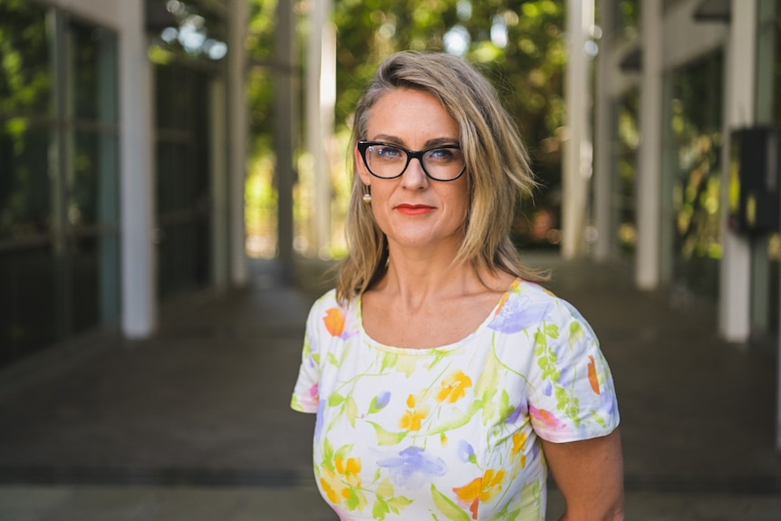 Una mujer rubia con gafas en vestido floral mirando a la cámara