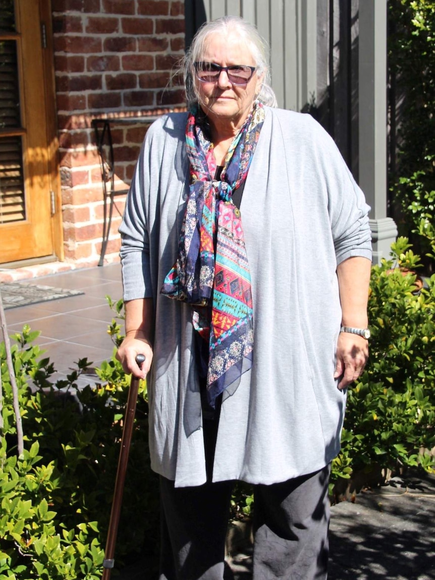 Heather Carey standing in front of her house leaning on a walking stick