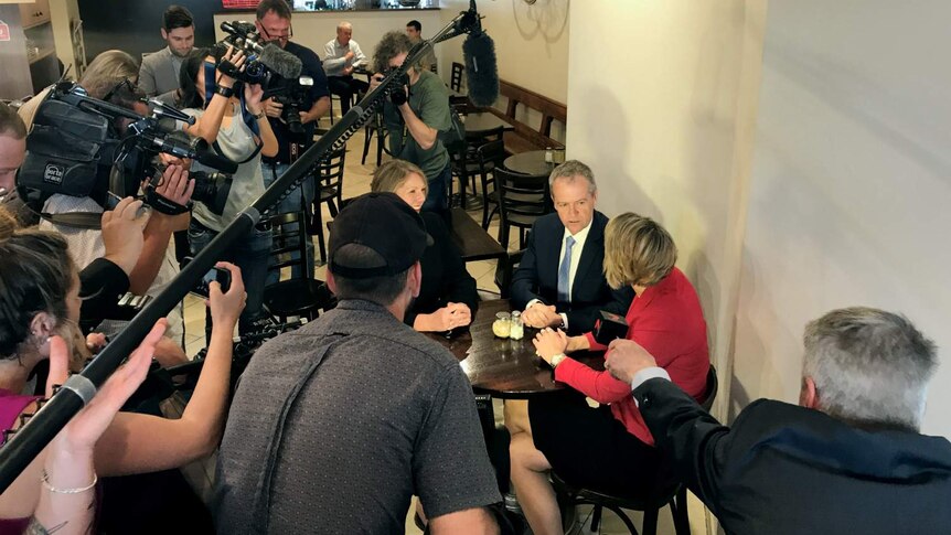 Two people sit at a table surrounded by media.