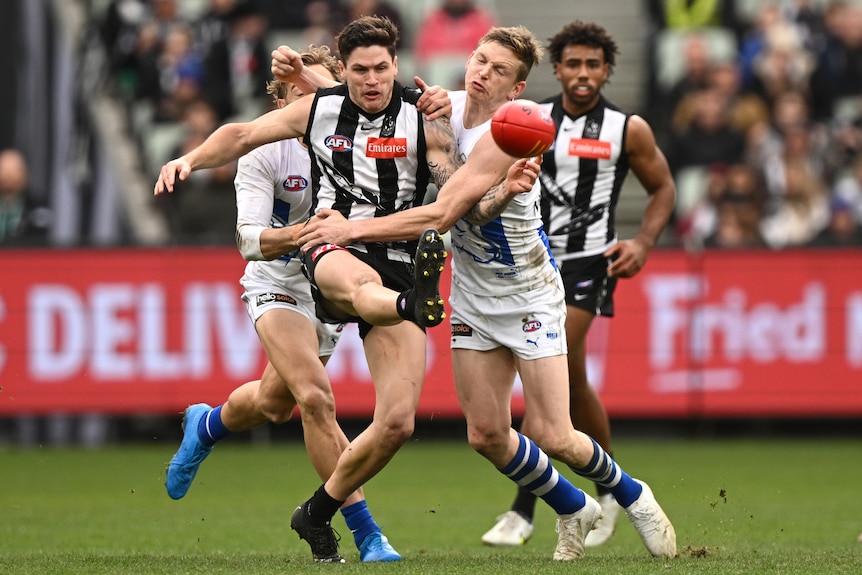 Un jugador de la AFL de Collingwood patea el balón mientras un oponente de North Melbourne lo aborda.