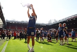 Footballer parades trophy in front of fans, and teammates, in a stadium