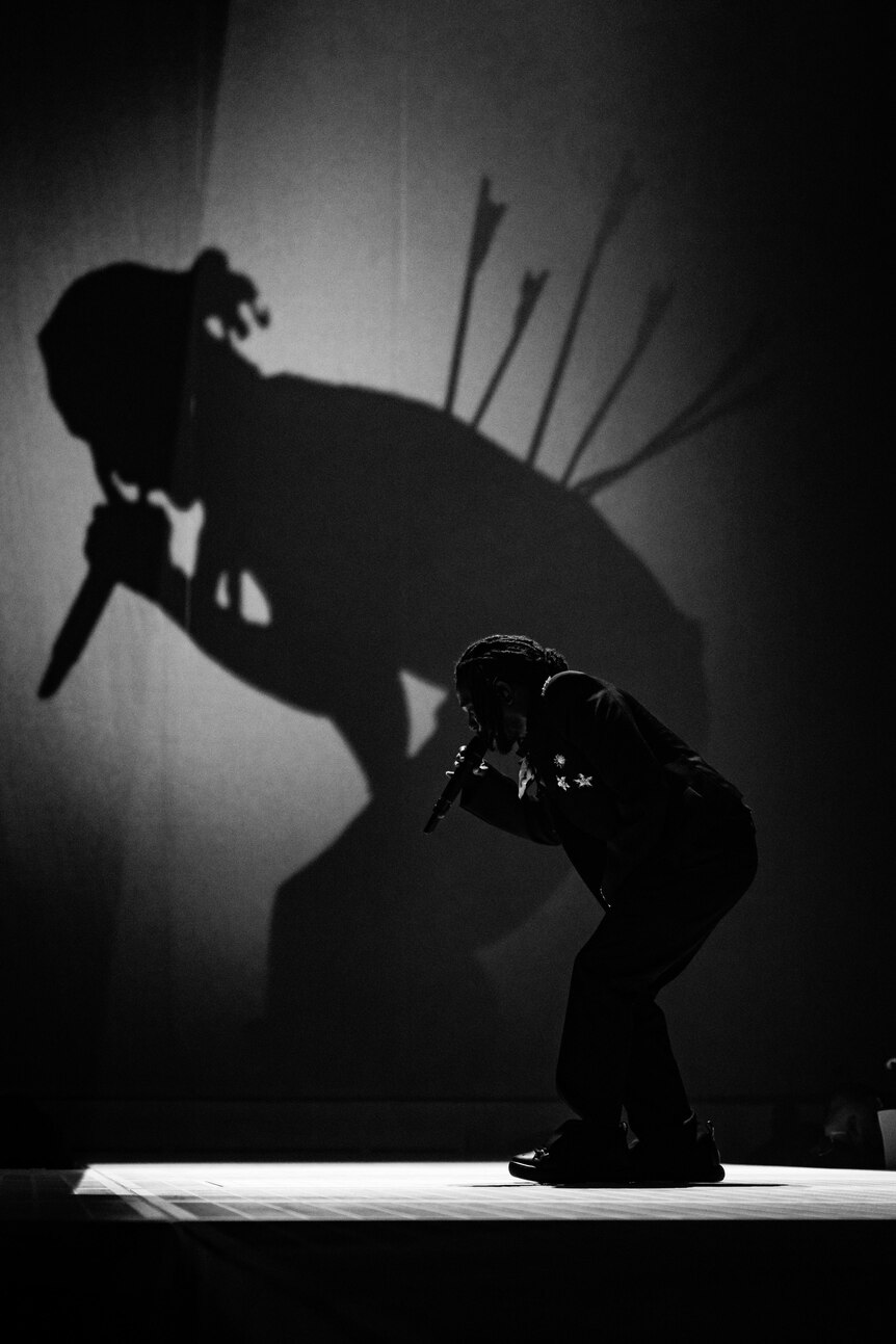 Kendrick Lamar performs live against a giant silhouette with arrows in its back