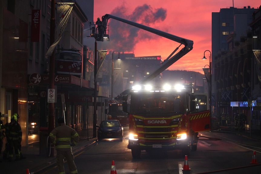 A firetruck is silhouetted by a pink sky as the sun rises over a city