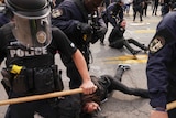 Police detain protesters as one man is seen laying on the ground with his hands cuffs behind his back.