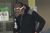 A man in a hoodie and sunglasses looks down.