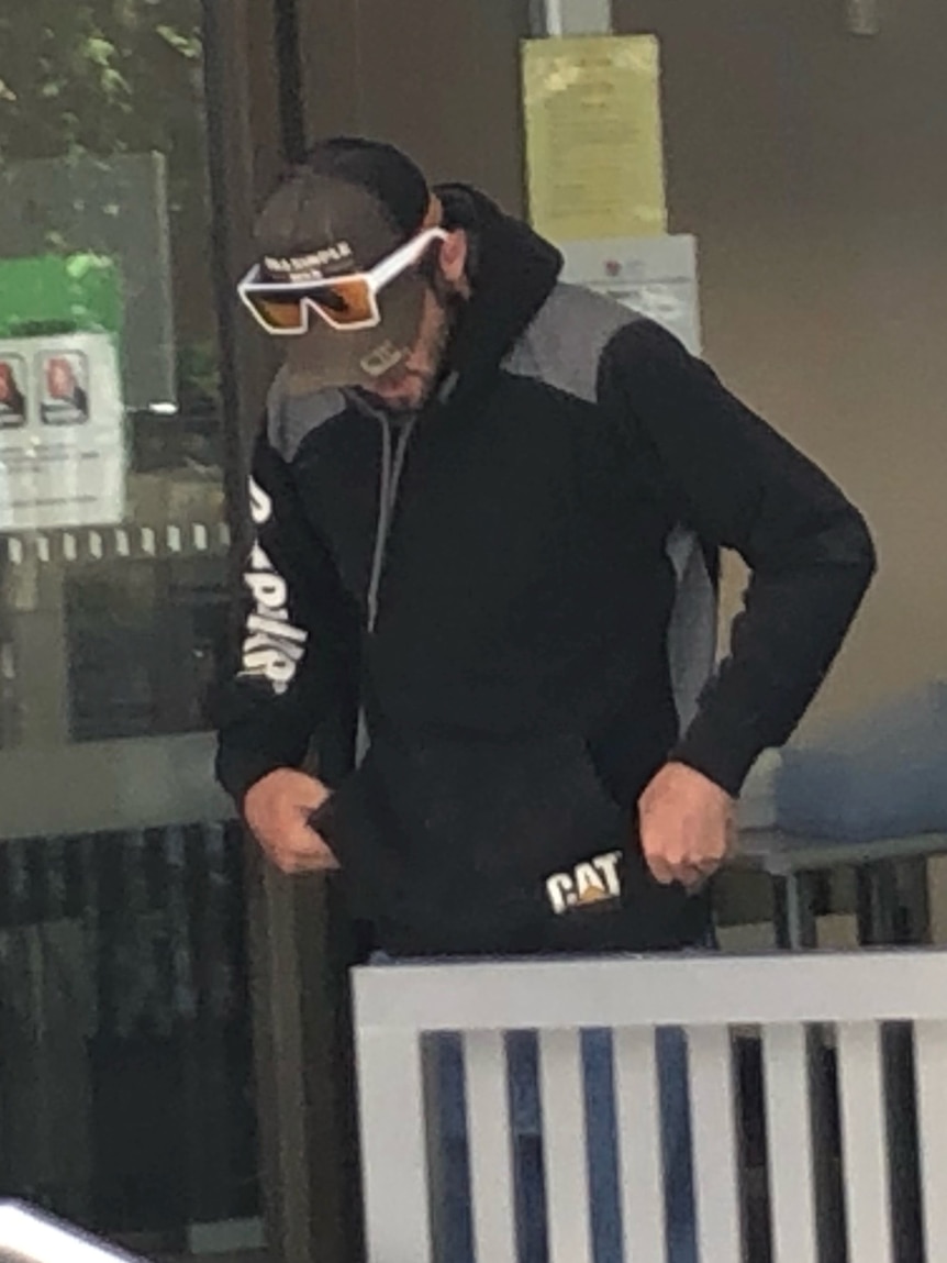 A man in a hoodie and sunglasses looks down.