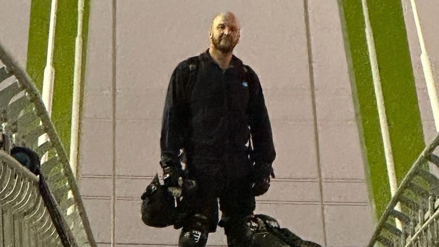 Man black riding gear with unicycle at his side