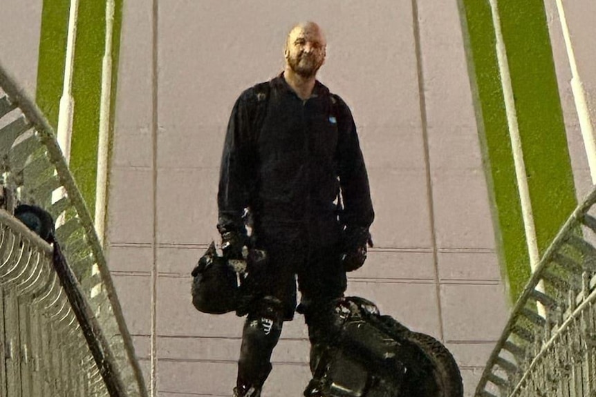 Man black riding gear with unicycle at his side